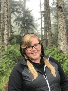 Program Coordinator Alexis Barton, smiling in front of a northwest forest background.