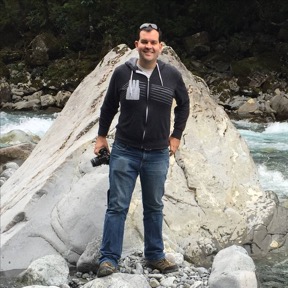 Glen Leverich standing beside a stream, in front of a large rock.