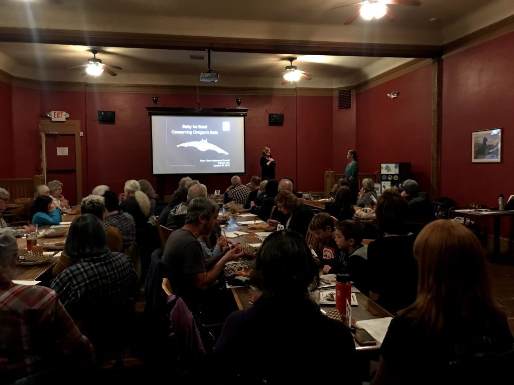 Room full of people with large presentation screen.