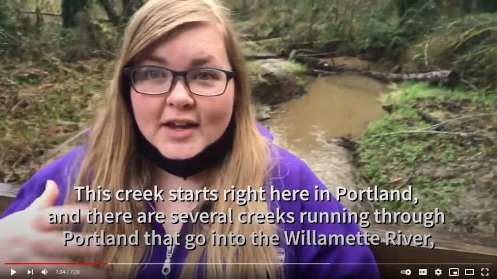 A screenshot of a video, where TCWC'S Coordinator stands on a bridge with Tryon Creek in the background.
